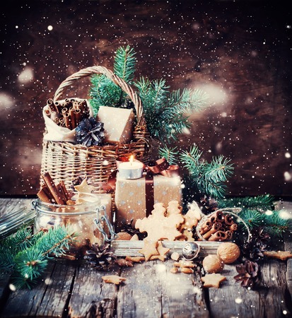 Festive Gifts with Boxes, Coniferous, Basket, Cinnamon, Pine Cones, Walnuts on Wooden Background. Vintage Style with Drawn Snowの写真素材