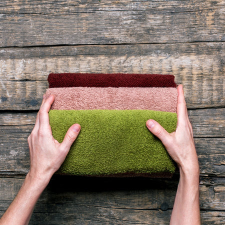 female hands holds stack bath towels colorful cotton terry textile background closeupの写真素材