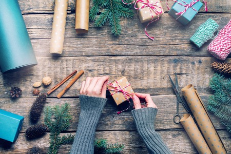 Female Hands Packing Christmas Gifts in Vintage Beige Blue Paper and Natural Decor Fir Branches Cones Cinnamon on Wooden Retro Desk. Top View Flat Layの写真素材