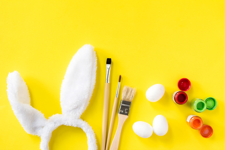 preparation to holiday. decorative Easter eggs decorated paints. cute little white eggs and bunny ears furry costume toy flat lay top view yellow backgroundの写真素材