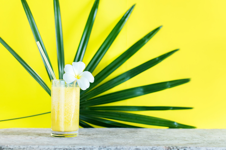 Fresh Color Juice Smoothie from Tropical Yellow Fruits in Glass with Straw Foreground Palm Leaf Background Diet Conceptの写真素材