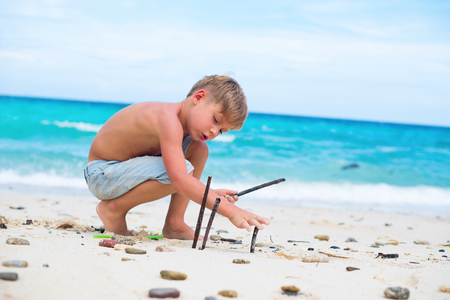 boy playing with natural sticks. blue sea white sand. tropical travel dreams concept. child connected to nature. copy spaceの写真素材