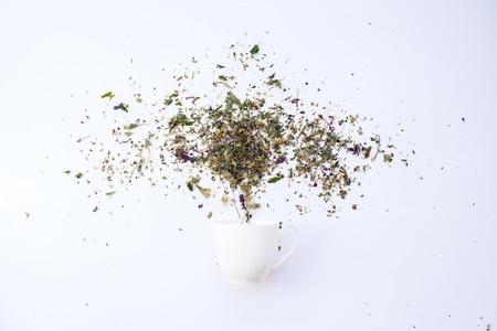 Cup and dry leaves herbal tea scattered on white background.の写真素材