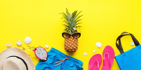 Stylized hero fruit major pine apple in glasses on a vacation. Set beach things accessories hot season hat, bathing suit, shorts, bag yellow background. Flat creative concept of travel holidaysの写真素材