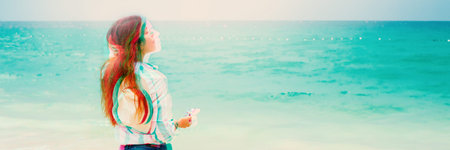 Beautiful happy young girl with long hair blowing on the wind standing on beach, looking on sea....