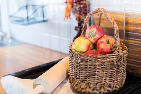 White kitchen vintage interior accessories. Apples in wattled basket. Chopping board and peppers stand on table top. Vintage country styleの写真素材