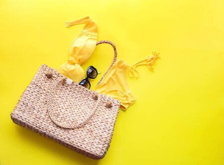 Wattled bag and women's bathing suit on yellow background. Summer time top view flat lay. Copy space single object banner conceptの写真素材