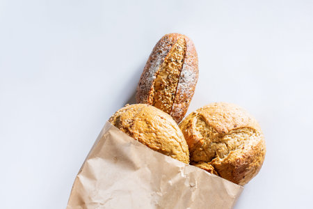 Whole grain bread with seeds in ecology paper bag on light gray background. Top view flat lay....