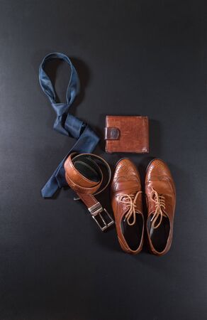 Set men classic accessories blue color tie, brown leather wallet, belt, shoes on black background. Top view. Flat layの写真素材