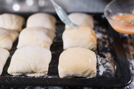 Chef hand smearing samsa pasties with egg yolk before putting the pasties in the oven at home. Stay and cooking at home. Quarantine. Isolation. Homemade. Uzbek cuisine.の写真素材