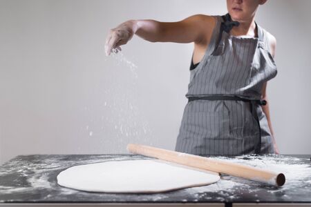Young woman pouring flour on the dough for rolling dough with long pin at home. Preparation of pastry for samsa making. Stay and cooking at home. Quarantine. Isolation. Homemade. Uzbek cuisine.の写真素材