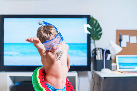 Boy in mask and snorkel dive imitating swimming near TV at home. Boy is having fun in mask and...