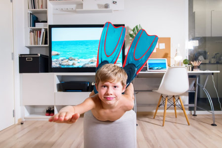 Boy in flippers having fun and imitating swimming into the sea near TV. Stay at home. Interior....