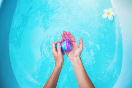 Woman holding a violet bomb in bathtub. Blue waterの写真素材