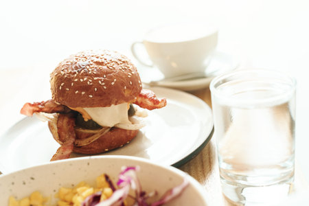 hamburger with bacon, cheese and sesame on white plate with coffee