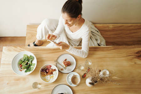Woman at the cafe eating her breakfast and using phoneの写真素材