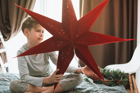 Boy is decorating home and window for Christmas with red star. Magic of winter holidaysの写真素材
