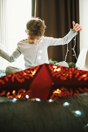 Boy is decorating home and window for Christmas with garland and red star. Magic of winter holidaysの写真素材