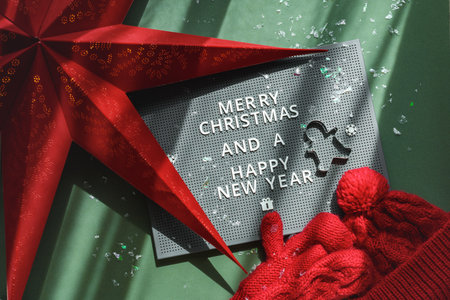 Typesetting plastic board with Greeting, red star lamp and metal shape gingerbread men on green background. Christmas decoration. Sun light.の写真素材