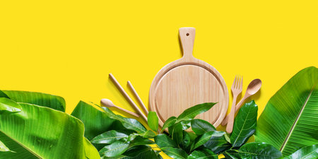 Mock up wooden chopping board with tropical palm leaves on yellow background. Flat lay top view....
