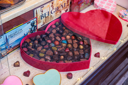 Heart-shaped red gift box filled with assorted Belgian chocolates on a shop counter, featuring...