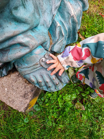 Close-up of a toddler s hand gently touching the weathered foot of a blue-green statue outdoors, captured from above, symbolizing curiosity, connection, and discovery in natureの写真素材