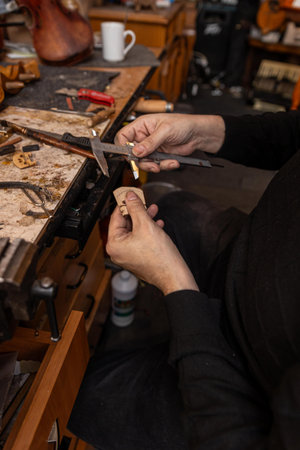 A skilled luthier repairs a violin amidst a cluttered workshop filled with tools, wood, and...