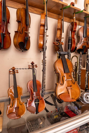 A row of polished violins hangs along wooden racks in a rustic workshop. Warm lighting highlights...