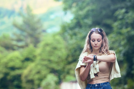 a young woman tourist with long wavy hair looks at her smart watch-phone while hikingの写真素材