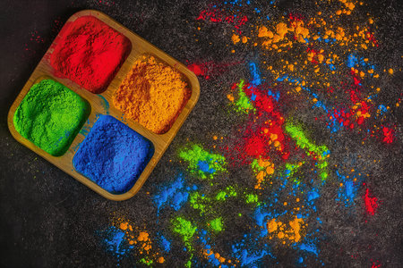 Organic multicolored bright colors of Holi in different colors in a wooden plate on a dark background for the celebration of the Holi festival, view from aboveの写真素材