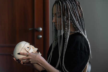 A young bright girl in dark clothes, with dreadlocks on her head, holds a skull in her hands. Generation z, gothic styleの写真素材