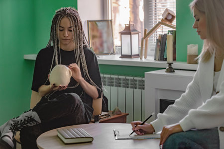 a female psychologist works in her office with a young client with dreadlocks on her head, who is holding a mock-up of a skull. Problems of generation z in life, in communication.の写真素材
