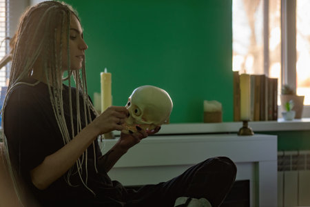 A young bright girl in dark clothes, with dreadlocks on her head, holds a skull in her hands. Generation z, gothic styleの写真素材