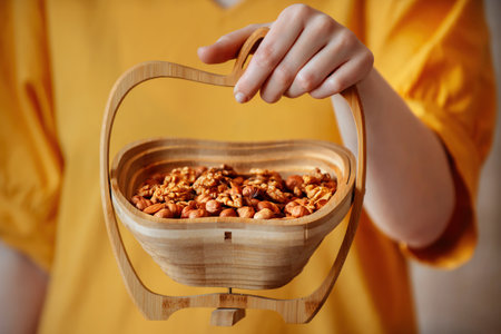 female hands hold close-up wooden basket with nut mix, almonds, hazelnuts, walnutの写真素材