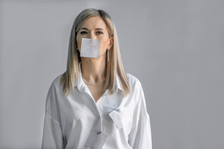 a blonde woman, a white sheet of paper for text is pasted on her mouth. The ban on the expression of feelings and emotionsの写真素材