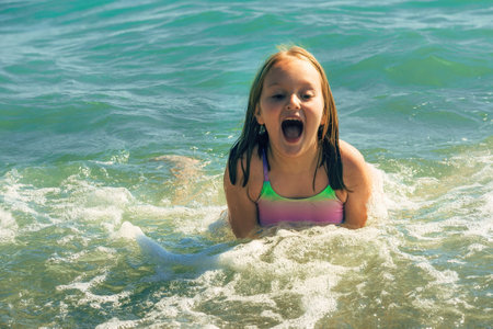 a little girl in a swimsuit swims cheerfully in the sea on a warm summer sunny dayの写真素材