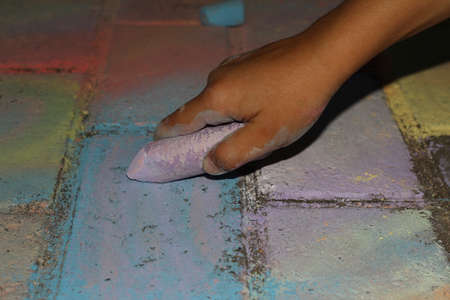 A child's hand holds Crayons. Drawings on the road. Children's entertainment.の写真素材