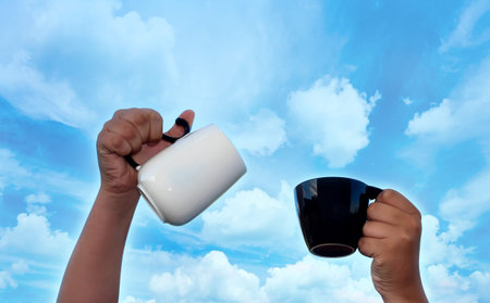 Two hands with cups of tea against the sky.の写真素材