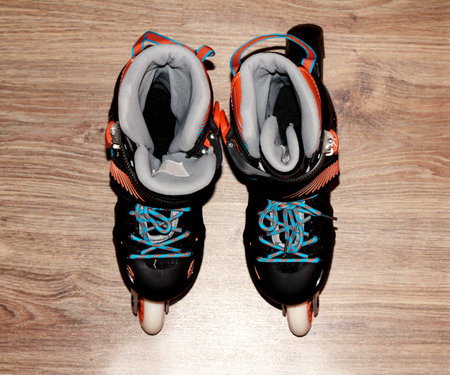 Roller skates on a wooden background. Roller skates are black and blue with orange color.