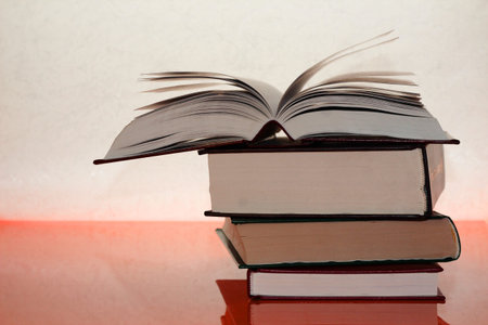 Three thick books on an orange table. A fan from the pages of a book. Open book. Background of...
