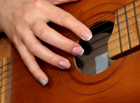 A woman's hand plays the guitar. A girl with a French manicure plays the guitar.