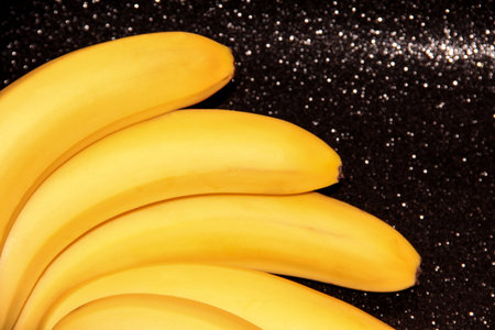 Bananas on a black background with bokeh and glitter. A fan of banana bunches.