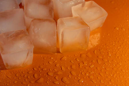 Pieces of ice on a bright background with water drops. Orange fresh background with ice flakesの写真素材