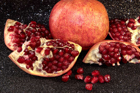 Juicy pomegranate on a black shiny background. Bright pomegranate berries.の写真素材