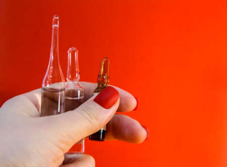 Ampoules in a woman's hand on a red background. A bottle of vaccine.の写真素材