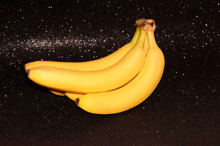 Bananas on a black background with bokeh and glitter.の写真素材