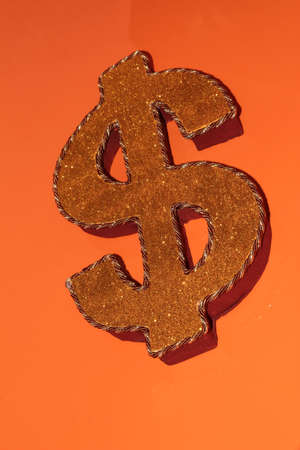Gold dollar sign with string and sequins. Dollar symbol on an orange backgroundの写真素材