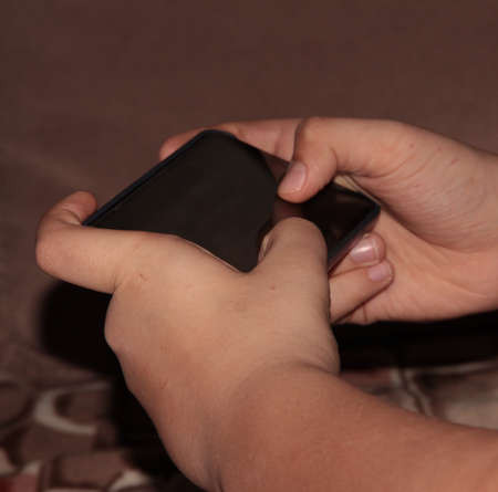 The child is holding a smartphone. Children's hands and phone.の写真素材