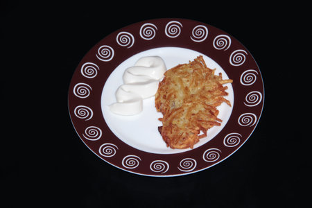 Potato pancakes with sour cream on a round plate on a black background