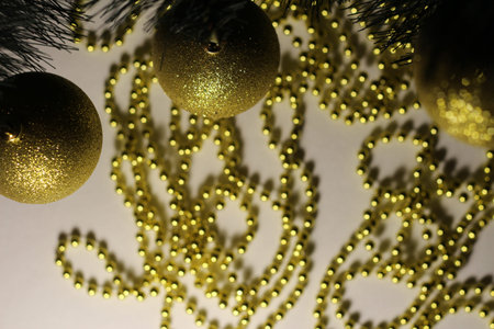 Golden Christmas balls on the branch of the Christmas tree, on the background of gold beadsの写真素材